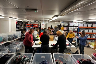 Photo of eight people sorting textiles into plastic boxes.