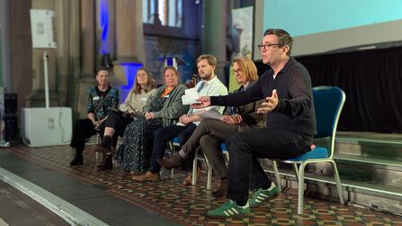 Andy Burham sits on a panel with five other people and is addressing the audience