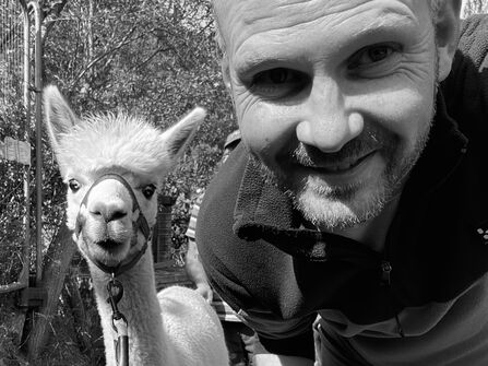 A black and white selfie of Roger with an alpaca
